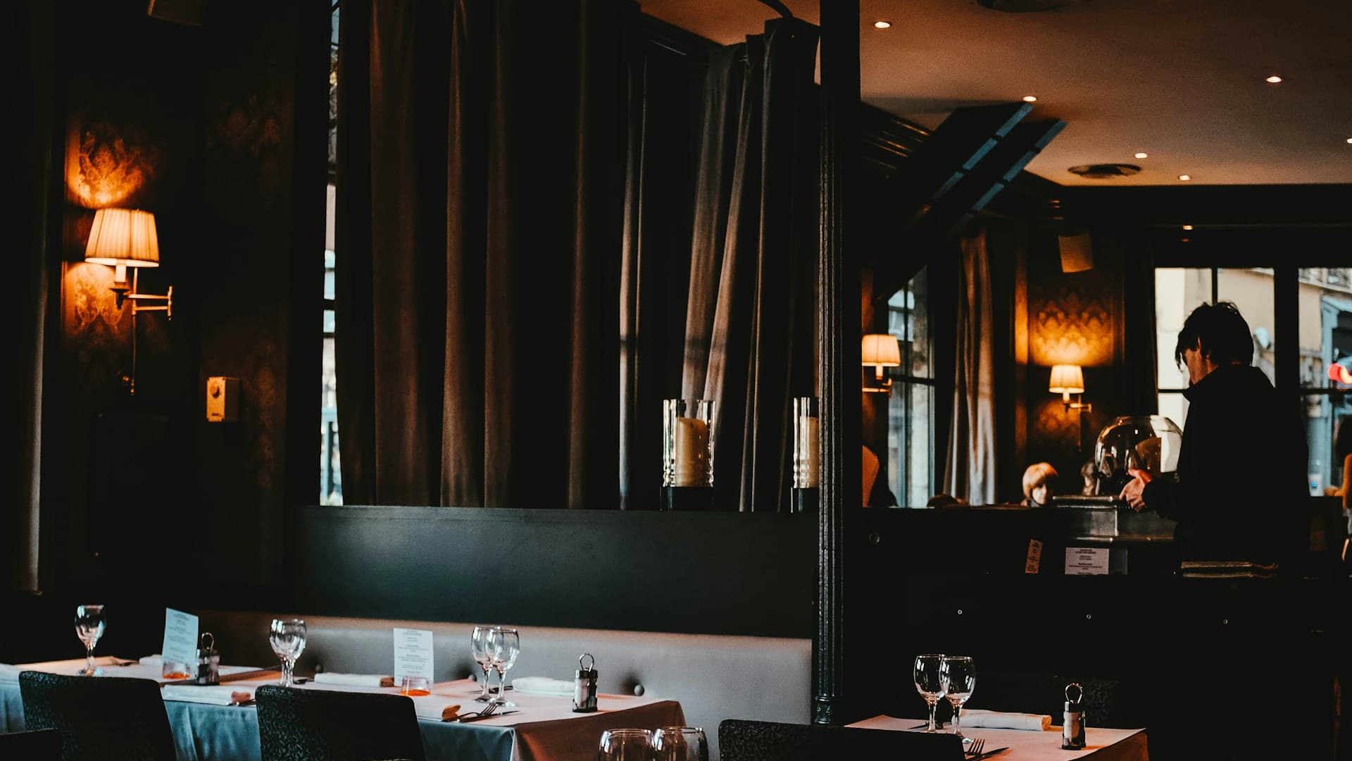 Intimate fine dining interior with warm ambient wall sconces, elegant table settings, and rich dark drapery